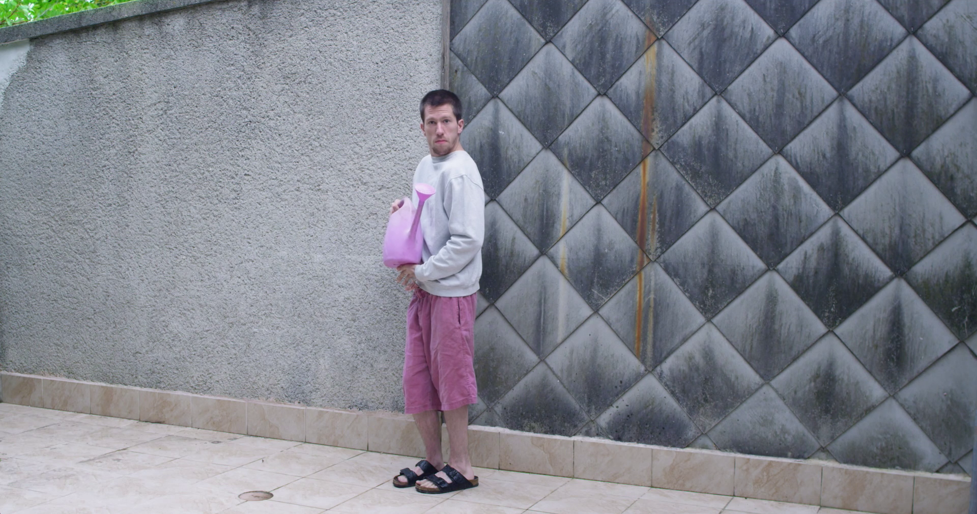 eszter galambos, Standing in front of the grey wall. Wearing pink shorts, having a pink waterpot. Cinematographer, operatőr: Eszter Galambos