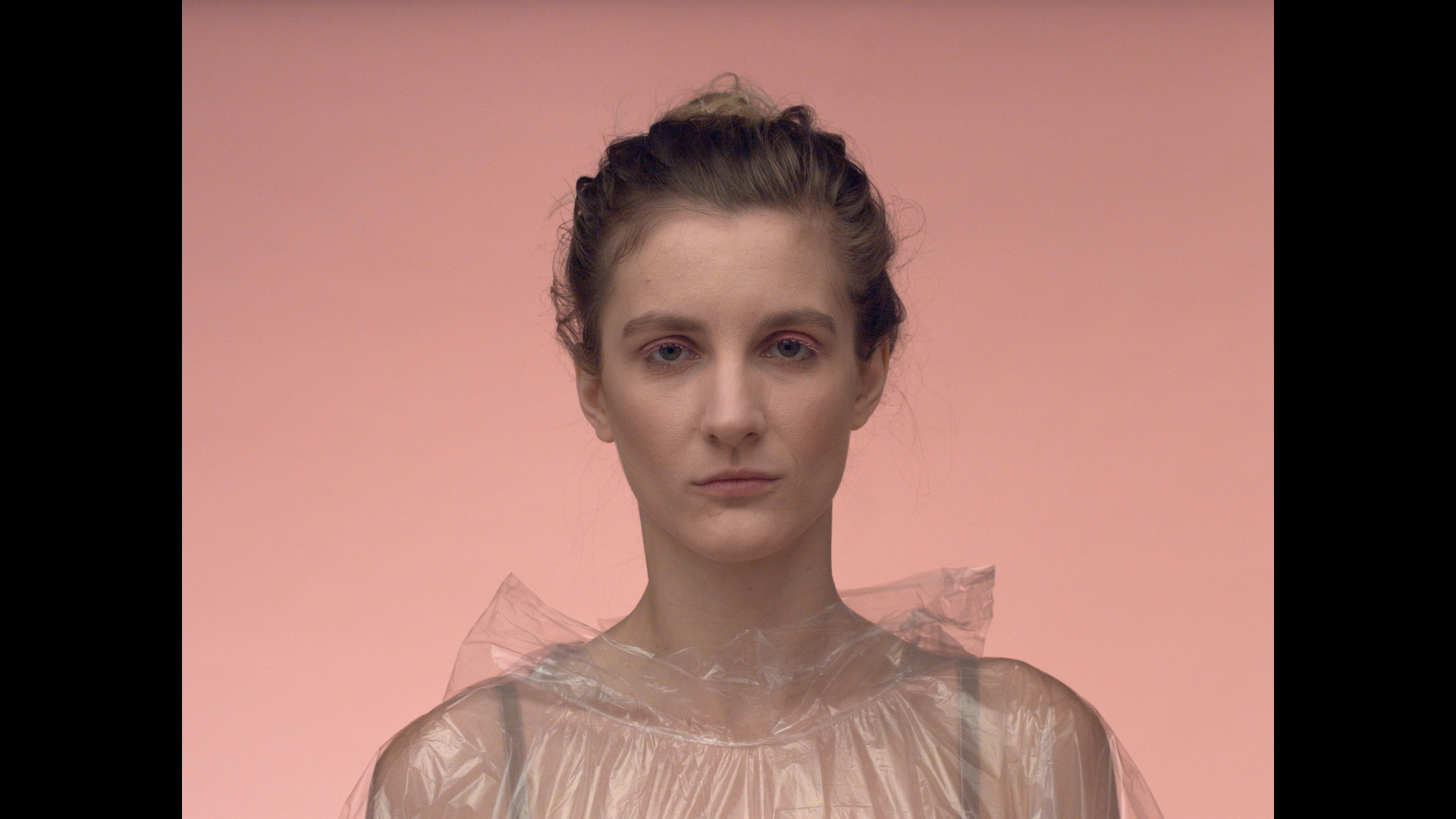 eszter galambos, Réka Ágnes Tóth in a raincoat in front of a pink background. Pastel pink. From the usic vide of Musica moralia: Architect. DOP, Cinematographer, operatőr: Eszter Galambos